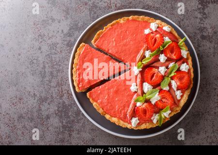 Tarte aux fraises et à la rhubarbe en tranches décorée de menthe et de crème fouettée sur une assiette sur la table. Vue horizontale du dessus Banque D'Images