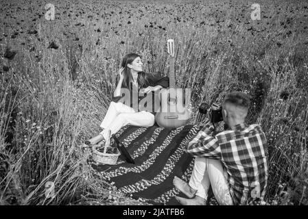 couple amoureux de faire des photos sur caméra avec guitare acoustique dans le champ de fleurs de pavot d'été, temps libre. Banque D'Images