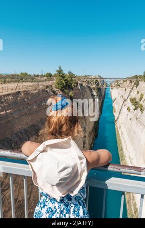 Une jeune fille regarde la côte du canal de Corinthe, le bord de mer gauche brille dans un lever de soleil doré, la droite est dans l'ombre, le contour du pont et le ciel bleu sur l'arrière-plan, Banque D'Images