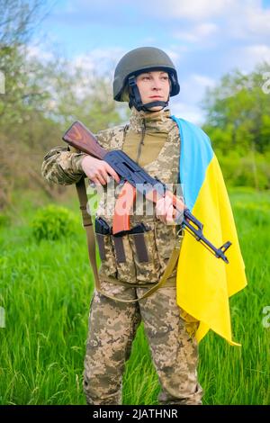 Soldat féminin avec arme à feu et drapeau ukrainien sur l'épaule, regardant loin Banque D'Images