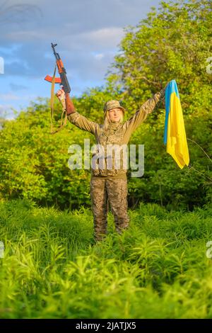 Soldat féminin avec arme et drapeau ukrainien dans les armes levées regardant loin Banque D'Images