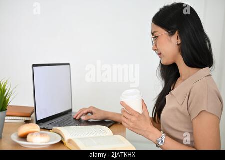 Belle jeune femme asiatique étudiant à distance travaillant au café, faisant des devoirs, utilisant un ordinateur portable, recherchant des informations sur t Banque D'Images