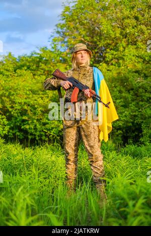 Femme pleine longueur soldat avec arme à feu et drapeau ukrainien sur l'épaule en regardant loin Banque D'Images