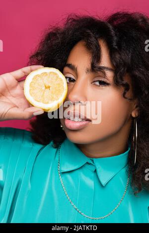 brunette femme afro-américaine tenant un demi citron près du visage isolé sur rose Banque D'Images