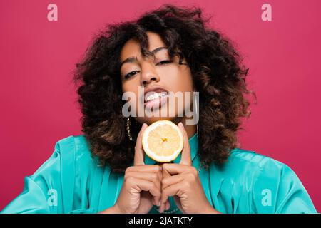 femme afro-américaine maurique tenant un demi citron et regardant la caméra isolée sur rose Banque D'Images