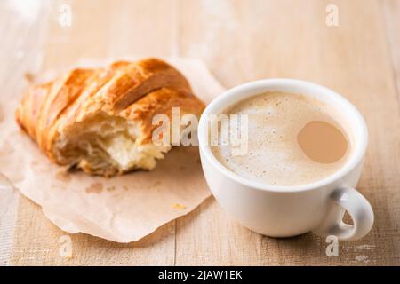 Cappuccino, café et croissant sur une table en bois, croissant manquant de bouchée Banque D'Images