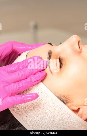 Le cosmétologue aux mains gantées applique un masque hydratant avec de la crème exfoliante sur le visage de la femme. Traitement de la cosmétologie du visage. Procédures de soin du visage Banque D'Images