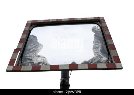 Gros plan d'un miroir de trafic partiellement aveugle endommagé et décoloré vu de l'oblique ci-dessous avec cadre blanc fissuré rouge sur fond blanc Banque D'Images