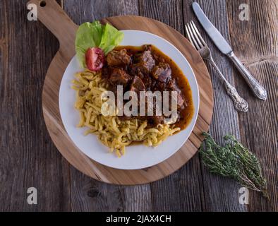 Goulash aux nouilles spaetzle sur une assiette isolée sur une table en bois avec espace de copie Banque D'Images