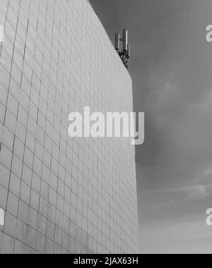 Photo en noir et blanc le mur extérieur d'un bâtiment moderne de style commercial, lambrissé de tuiles, sur le toit des antennes modernes contre le ciel Banque D'Images