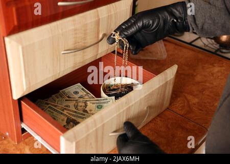 Vêtement noir et gants de cambriolage, voir dans l'étagère ouverte de la cuisine. Le voleur sort le collier doré d'une étagère de cuisine Banque D'Images