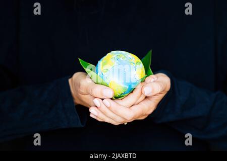 Jeune femme tenant une petite planète entre les mains sur fond noir. Écologie, environnement et concept du jour de la Terre. Banque D'Images