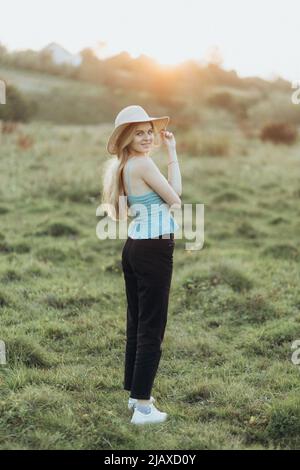 une femme en veste et chapeau profite du coucher de soleil seul Banque D'Images