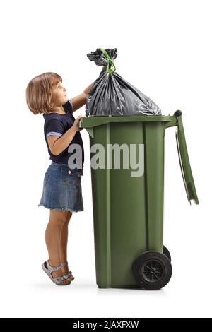 Photo pleine longueur d'une petite fille mettant un sac de déchets dans un bac en plastique isolé sur fond blanc Banque D'Images