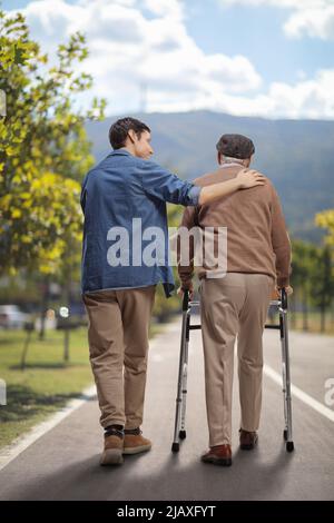 Vue arrière photo d'un jeune homme aidant un homme âgé avec un marcheur à l'extérieur Banque D'Images