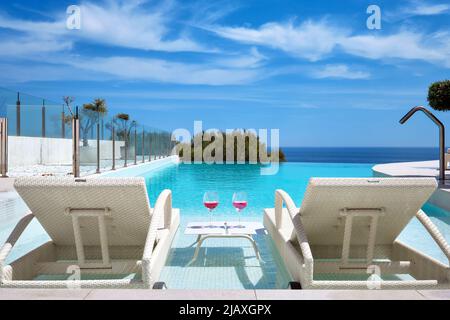Deux verres avec cocktails sur la table entre les chaises longues chaises longues sur la piscine, mer, ciel bleu sur fond de piscine. Vacances d'été, concept de détente Banque D'Images