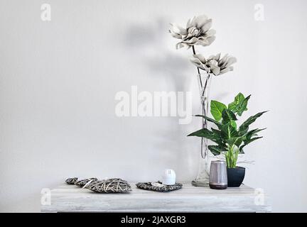 Fleurs artificielles en pot vert naturel et gris dans un vase avec de jolis accessoires maison sur une table sur fond de mur blanc, espace de copie intérieur Banque D'Images