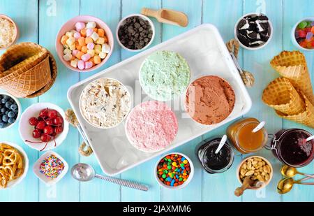 Buffet de glaces d'été avec une variété de saveurs et des garnitures sucrées. Scène de table avec vue sur le dessus sur fond de bois bleu. Banque D'Images