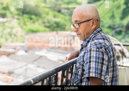 gros plan d'un latin âgé à la peau marron qui va sur le balcon de sa maison pour regarder ce qui se passe dans la rue de son quartier, quie Banque D'Images