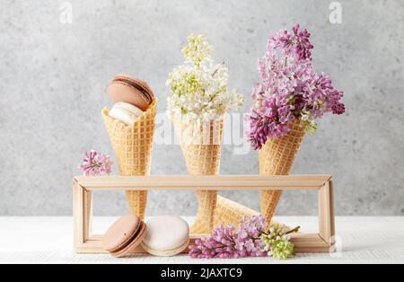 Divers biscuits macarons dans des cônes de crème glacée et des fleurs de lilas Banque D'Images