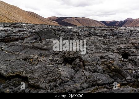 Le roche volcanique grossière et torsadée en forme de corde du volcan Geldingadalir est empilée densément au premier plan ; les pentes brunes du bassin de la vallée de la péninsule de Reykjanes près de Grindavík, en Islande, s'élèvent derrière elle. Le volcan a été actif de mars à septembre 2021 et était alors le plus jeune d'Islande. Banque D'Images