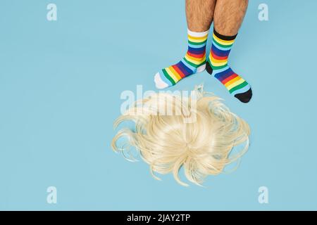 Photo minimale d'un homme portant des chaussettes arc-en-ciel avec perruque blonde sur le sol, sur fond bleu pastel, espace copie Banque D'Images