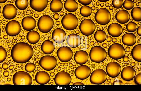 Texture créée avec un gros plan avec des gouttes d'eau dorées de différentes tailles sur une surface lisse Banque D'Images