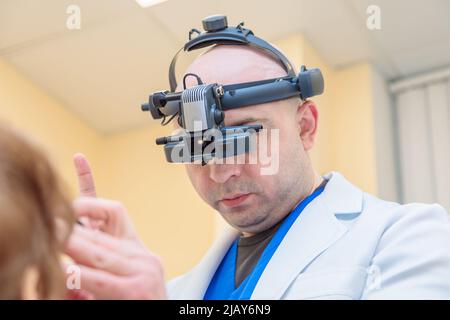 Un ophtalmologiste mâle vérifie la vue d'une femme adulte avec un ophtalmoscope binoculaire. Banque D'Images