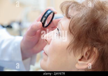 Un ophtalmologiste mâle vérifie la vue d'une femme adulte avec un ophtalmoscope binoculaire. Banque D'Images