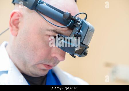 Un ophtalmologiste mâle vérifie la vision d'un patient à l'aide d'un ophtalmoscope binoculaire. Banque D'Images