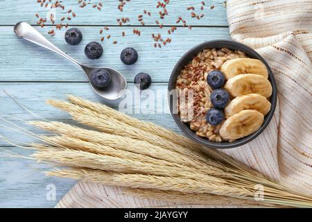 Flocons d'avoine avec bleuets et bananes dans un bol bleu foncé sur une table peinte en bleu. Porridge de céréales pour une alimentation saine. Banque D'Images