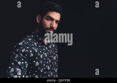 Beau barbu latino-américain regardant sévèrement dans l'espace de copie de l'appareil photo noir arrière-plan studio tourné de gros plan moyen. Photo de haute qualité Banque D'Images