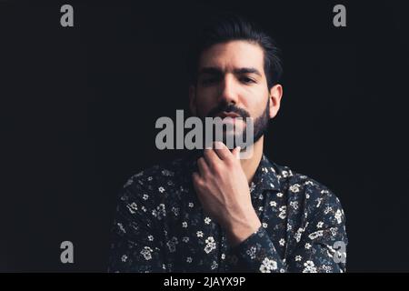 Homme barbu d'Amérique latine beau contact avec son menton regardant sévèrement dans l'espace de copie de caméra arrière-plan noir studio tourné de gros plan moyen. Photo de haute qualité Banque D'Images