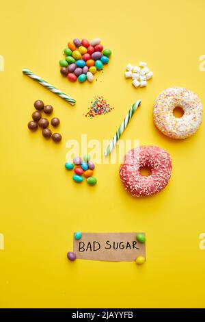 Bad Sugar concept: Divers bonbons malsains tels que des beignets, des méduses et des canes de bonbons sur fond jaune Banque D'Images