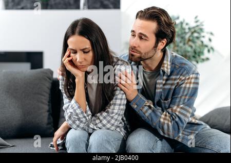 Un couple marié réconcilie après une querelle. Un homme et une femme sont assis sur un canapé, un homme demande pardon à une femme, ou console elle, la fille brune est bouleversée ou offensé par son mari Banque D'Images