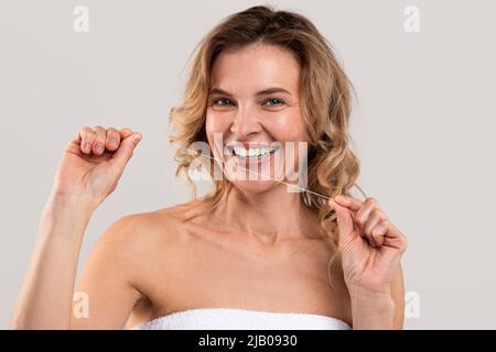 Santé bucco-dentaire. Portrait d'une femme d'âge moyen souriante utilisant un fil dentaire Banque D'Images