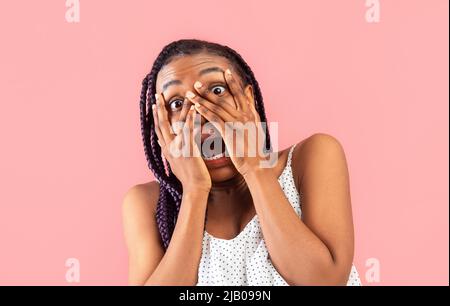 Femme noire millénaire se sentant effrayée, criant dans la peur, couvrant son visage avec les mains, peeking à travers les doigts Banque D'Images