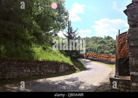 Tourner dans une route pavée en montée dans une forêt bordée par la clôture d'un chantier de construction Banque D'Images