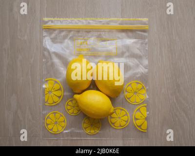 Trio de citrons frais placés sur un sac de stockage de nourriture ziplock sur un fond de bois clair Banque D'Images