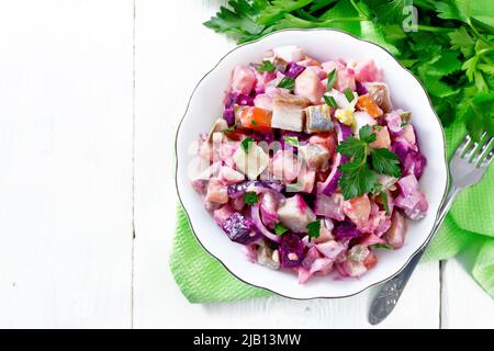 Salade de rosoli finlandais de hareng, betteraves, pommes de terre, concombres marinés ou marinés, carottes, oignons et œufs, assaisonnés de mayonnaise dans un bol sur bois Banque D'Images