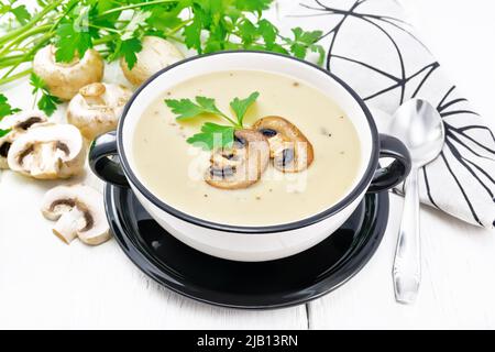 Soupe de purée de champagnes, pommes de terre, oignons et crème dans un bol, une serviette de cuisine, persil et une cuillère sur fond de bois Banque D'Images