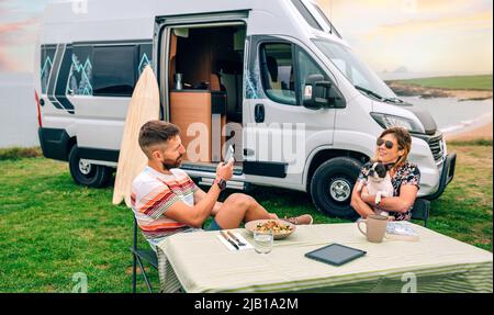 Homme prenant la photo à une femme qui embrasse un chien avec une camionnette et la plage en arrière-plan Banque D'Images