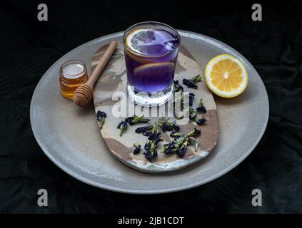 Jus de paaflower aux papillons de couleur bleue et violette (Clitoria) mélangé avec de la limonade et de la glace, décoré de fruits au citron jaune, émincés avec du miel et Banque D'Images