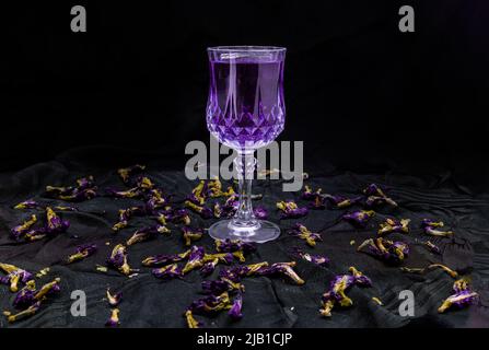 Fleur violette jus de pois papillons (Clitoria) en verre et fleurs de pois papillons sèches sur fond sombre. Boisson santé à base de plantes détoxiques, espace pour te Banque D'Images