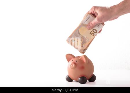 détail d'une main insérant un billet de cinquante euros dans une banque de porc, concept pour les affaires et économiser de l'argent sur fond blanc. Banque D'Images