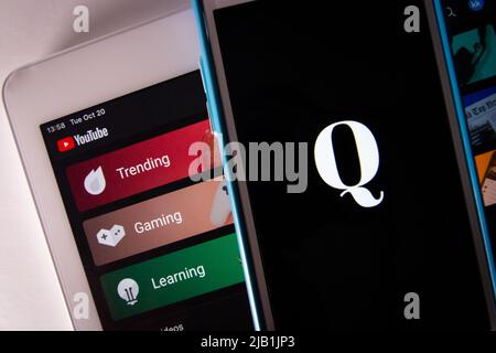 Kumamoto, JAPON - octobre 20 2020 : logo Qanon sur iPhone avec YouTube sur tablette. Qanon est un groupe de conspiration d'extrême-droite Banque D'Images