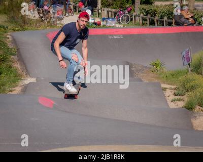 Merville, France, mai 2022. Un homme en Jean et un chapeau rouge fait un skateboard sur la piste du parc. Journée ensoleillée, détente, style de vie sportif Banque D'Images