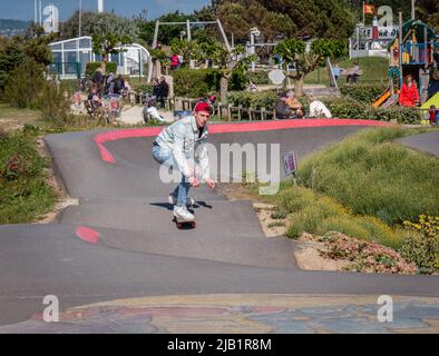 Merville, France, mai 2022. Un homme en Jean et un chapeau rouge fait un skateboard sur la piste du parc. Journée ensoleillée, détente, style de vie sportif Banque D'Images