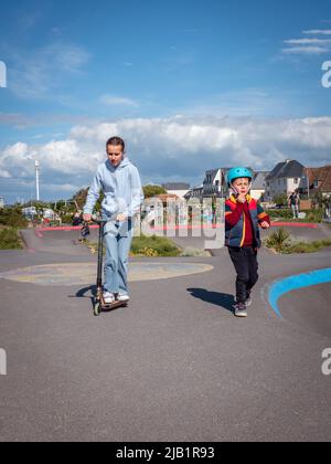 Merville, France Mai 2022. Les enfants portant des casques de scooter sur une piste de sport lors d'une journée ensoleillée, vacances d'été Banque D'Images