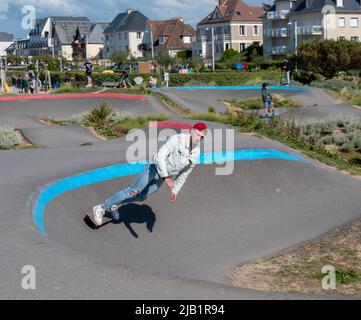 Merville, France, mai 2022. Un homme en Jean et un chapeau rouge fait un skateboard sur la piste du parc. Journée ensoleillée, détente, style de vie sportif Banque D'Images